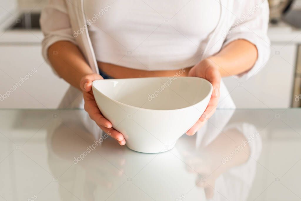 Woman with empty glass bowl in her hands in the kitchen. No food, diet, Rising food, concept