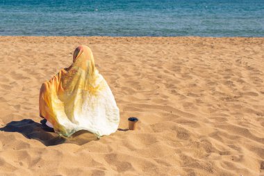 Renkli bir başörtüsü takmış, kumsaldaki kumsalda elinde bir fincan kahveyle gezen yalnız Müslüman kadın..