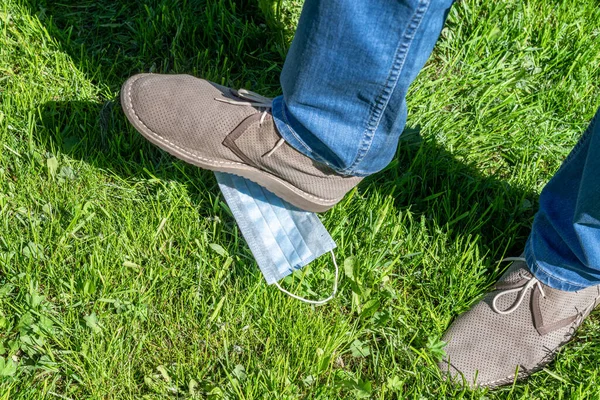 A man steps on a medical mask lying on the grass in the park. Over coronavirus. End of pandemic and quarantine.  End of the epidemic. Concept