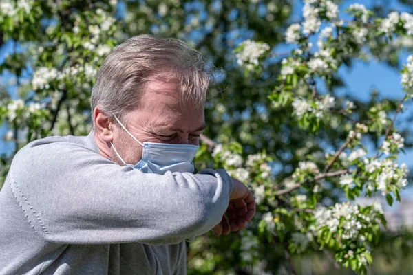 Egy Fehér Hajú Középkorú Férfi Orvosi Maszkban Tüsszentett Parkban Virágzó — Stock Fotó