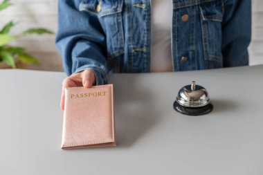 Otelde kayıt için pasaport kullanan bir kadın. Resepsiyonda gümüş antika zil var. Otel servisi. 