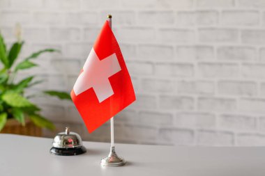 İsviçre 'nin ulusal bayrağı resepsiyonda fotokopi masasının üzerinde duran gümüş rengi bir zil. Otel servisi. Seyahat, turizm. Seçici odaklanma. Avrupa, Kavram.