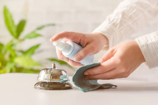 Hand of woman cleaning ringing bell on reception desk. disinfection spray, small towel. Protection from bacteria and virus. Keeping health of guests. Hotel service. Selective focus