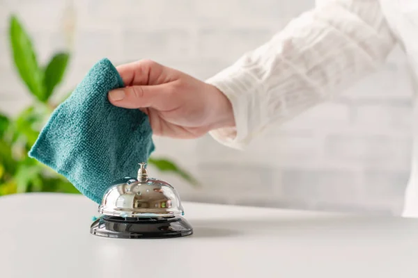 Hand of woman cleaning ringing bell on reception desk. disinfection spray, small towel. Protection from bacteria and virus. Keeping health of guests. Hotel service. Selective focus