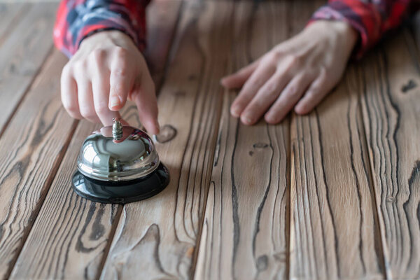 Hand of guest ringing in silver bell. on wooden rustic reception desk with copy space. Hotel, restaurant service. Selective focus