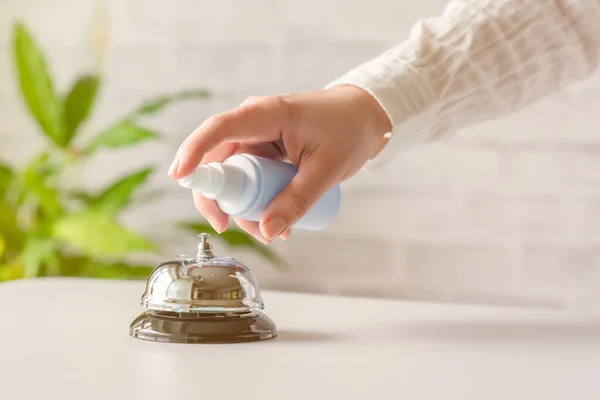 Hand of woman cleaning ringing bell on reception desk. disinfection spray, small towel. Protection from bacteria and virus. Keeping health of guests. Hotel service. Selective focus