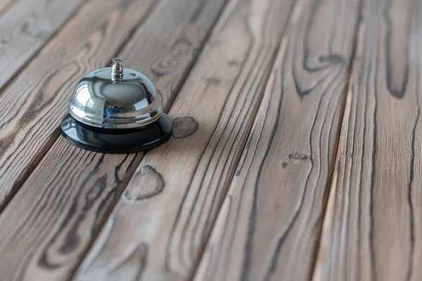 Silver vintage bell on wooden rustic reception desk with copy space. Hotel, restaurant.