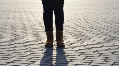 Çizmeli bir kız akşam ışığında kaldırımda duruyor..