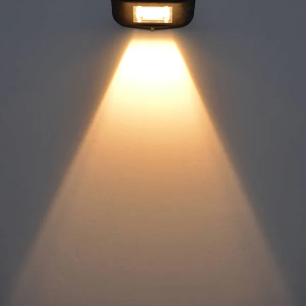 Uma pequena lâmpada de rua ilumina a parede. Um amplo feixe de luz é dirigido — Fotografia de Stock