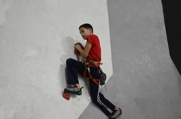 Un niño en una pared de escalada. El chico sube a la cima de la pared . — Foto de Stock