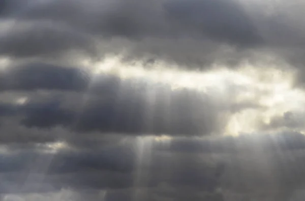 Nubes de lluvia de color: gris, azul oscuro. Luz blanca brilla detrás de las nubes . — Foto de Stock