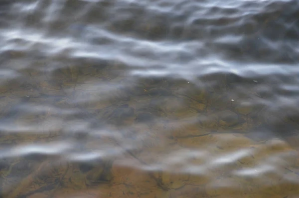 Il fondo del fiume è visibile attraverso le onde dell'acqua . — Foto Stock