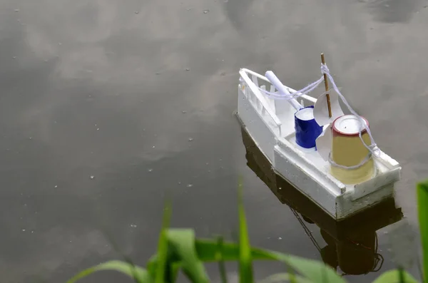 Bir çocuk kayığı, yeşil sazlıkların yanında, gölette yüzer. Bir çocuk tarafından yapılmış bir tekne bastondan yüzer. Oyuncak bir tekne resmi. Yukarıdan görünüşü.
