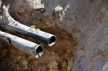 Çukurda iki metal boru var. Konsept: İnşaat işi, kaza, boruların değiştirilmesi, su tedarik boruları döşemesi.