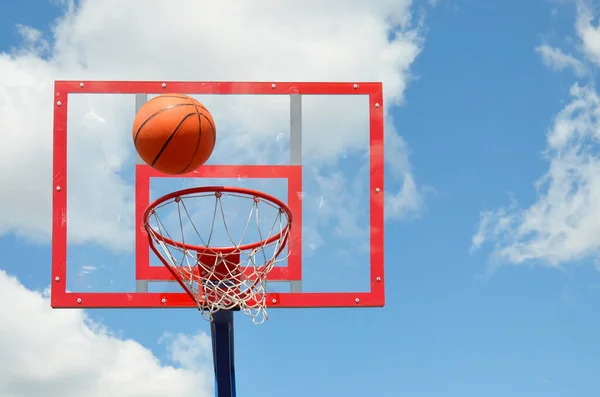 Bir basketbol topu gökyüzüne karşı açık bir alanda halka içine uçar.