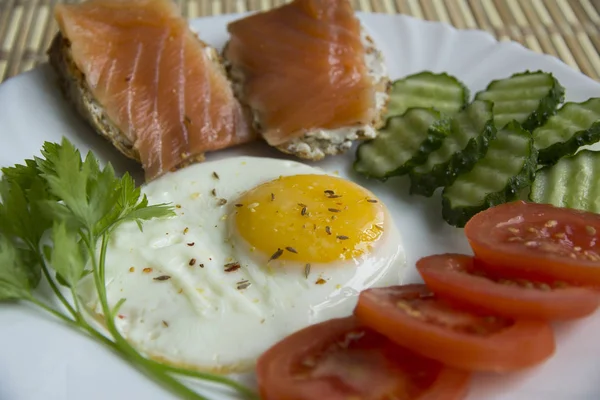 Fried eggs with spices, salmon, tomatoes, cucumbers, parsley