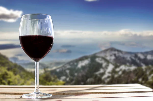 Glass of wine on Velebit mountains blur background in Croatia. Sunny view of glass of red wine overlooking mountains, Croatia