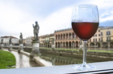Akşamları İtalya 'nın Padova kentinde Prato della Valle meydanında heykelleri olan kanal manzaralı bir kadeh kırmızı şarap.