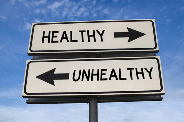 Unhealthy vs healthy. White two street signs with arrow on metal pole with word. Directional road. Crossroads Road Sign, Two Arrow. Blue sky background. Two way road sign with text.