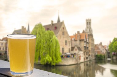 Belçika 'nın Bruges kentindeki tarihi evler, kanallar ve çan kulesi manzaralı bir bardak bira.. 