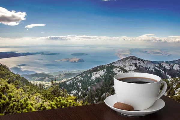 Cup of coffee with mountain landscape background. Coffee or tea on the top of mountain peak. Beautiful view of sea coast, islands and mountains during breakfast.