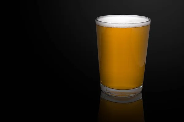 Cold craft beer isolated on black. Glass of light wheat beer with reflection on black background. Low key.