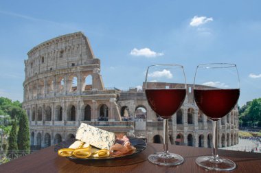 Roma, İtalya 'da Colosseum (Kolezyum) manzaralı iki bardak şarap. Farklı atıştırmalıklarla bir bardak kırmızı şarap. Jambonlu, dilimlenmiş, mavi peynirli tabak. Romantik kutlama..