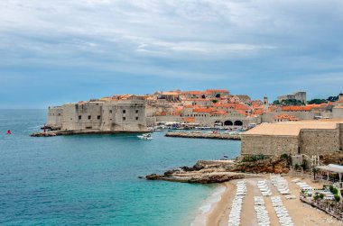 Dubrovnik kale duvarları, plaj ve turkuaz su manzarası. Dubrovnik şehir duvarları ve eski kasaba manzaralı ünlü Banje Sahili. Güzel mavi su ve sarı gönder.