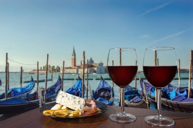 Venedik 'te gondollar ve San Giorgio Maggiore kilisesi manzaralı iki kadeh şarap. Farklı aperatiflerle bir bardak kırmızı şarap. Jambonlu tabak, dilimlenmiş.