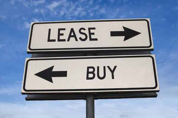 Lease vs buy. White two street signs with arrow on metal pole with word. Directional road. Crossroads Road Sign, Two Arrow. Blue sky background. Concept for own property versus borrow it.