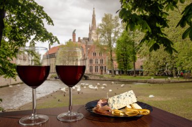 Belçika, Bruges manzaralı iki kadeh şarküteri çeşnili şarap. Farklı atıştırmalıklarla bir bardak kırmızı şarap. Jambonlu, dilimlenmiş, mavi peynirli tabak. Romantik kutlama..
