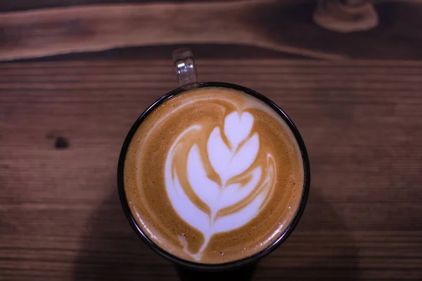 Une tasse de café avec motif de feuilles dans une tasse en verre sur fond en bois . — Photo