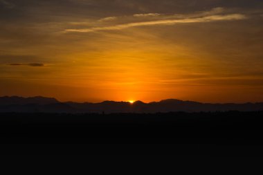 Altın gökyüzü ve güneş dağın siluetinin arkasında saklanıyor güzel günbatımının olduğu bir şehirde..