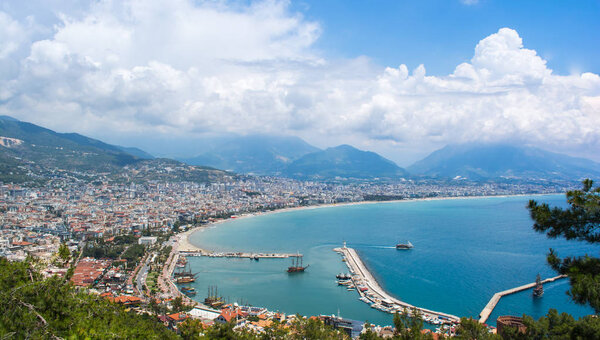 Sea surface with clouds on horizon and costline town with mountains on the background.