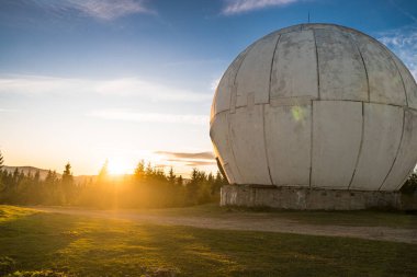 Kırmızı desenli beyaz küreler şeklinde eşsiz bir şekilde tasarlanmış eski radar istasyonu üzerinde dramatik bir gün doğumu..