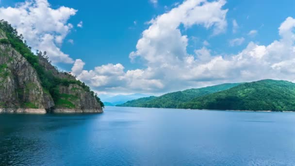 美妙的时间流逝视频与蓝色的湖水 高耸的岩石山和美丽的云 天空是蓝色的 云彩遮蔽了太阳 背景中的森林 — 图库视频影像