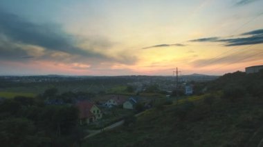 Güneşte boğulan bol tepeler. Evlerin çevreleri sık ağaçlarda ve büyüleyici bir günbatımında gizlidir.