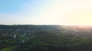 Ormanlardaki altın günbatımı bir dron üzerinde çekildi - güzel yaz manzarası, tepelerdeki ağaçlar, köy, evler, blu gökyüzü ve parlak güneş ışığı
