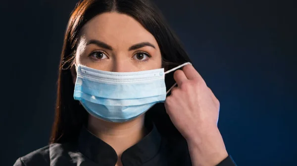 Siyah ve mavi arka planda güzel bir kız tıbbi bir maskeyi çıkarıyor. Corona virüsünün salgını hakkında bir başlık. Epidemy konsepti