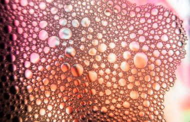 Sabun köpüklerinin makro damlaları ve pigmentleri mor arkaplanlı su yüzeyine düşer