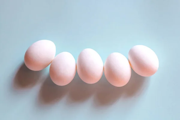 Beyaz tavuk yumurtaları mavi arka planda yatar..