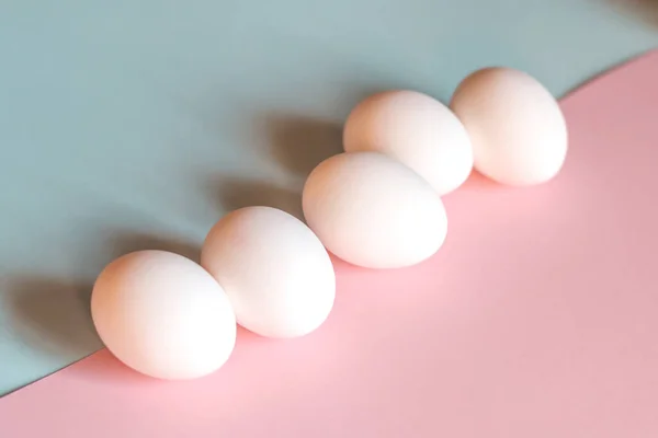 Beyaz tavuk yumurtaları mavi ve pembe arka planda yatar..