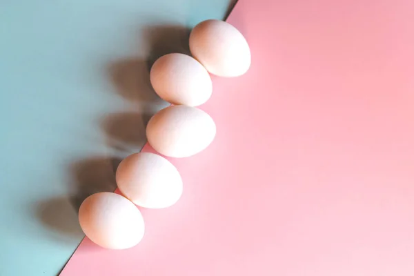 Beyaz tavuk yumurtaları mavi ve pembe arka planda yatar..