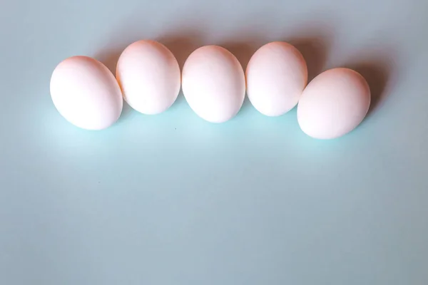 Beyaz tavuk yumurtaları mavi arka planda yatar..