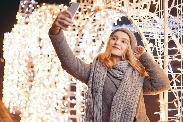 Una bella ragazza che fa selfie all'aperto davanti alle decorazioni natalizie . — Foto Stock