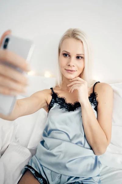 Ansicht von oben: attraktive junge Frau macht Selfie und lächelt, während sie zu Hause auf dem Bett sitzt. — Stockfoto