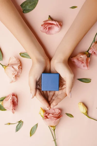 As mãos da fêmea carregam um pequeno presente entre rosas floridas, flat lay . — Fotografia de Stock