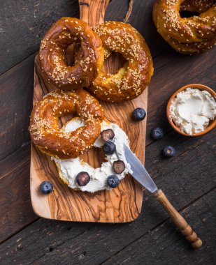 Krem peynirli bagel sandviçi ve ahşap masada yabanmersini.