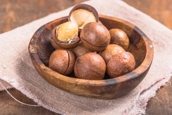 Pile noci di macadamia aperto kernel e conchiglie in sacchetto di iuta su woo — Foto Stock