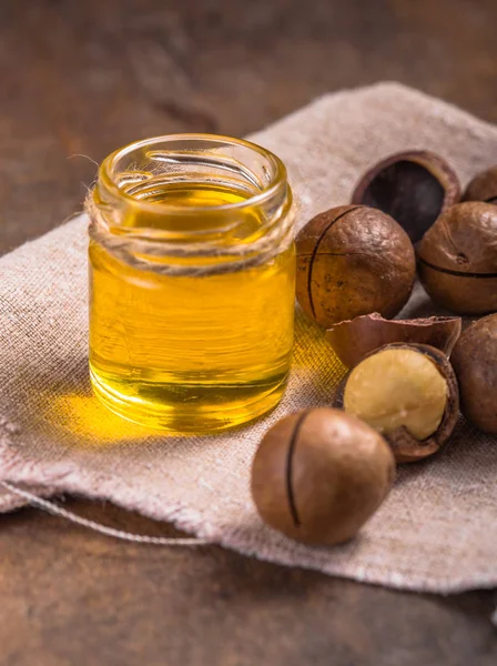 Nueces maduras de macadamia y una botella de vidrio con aceite natural — Foto de Stock